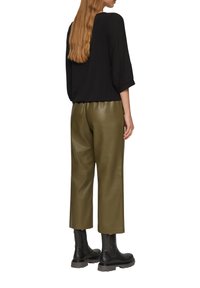 Haut noir à manches longues avec des manches texturées, associé à un pantalon large en simili cuir olive vert, taille haute, et des bottines noires.