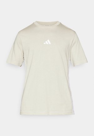 Bež majica s kratkimi rokavi iz mehke tkanine z okroglo izrezom, ki ima spredaj belo logotip Adidas in bele stranske črte.