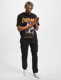Svart grafisk t-skjorte med "Tupac" tekst, med fargerik design. Svart cargo-bukse og hvite sneakers fullfører antrekket.