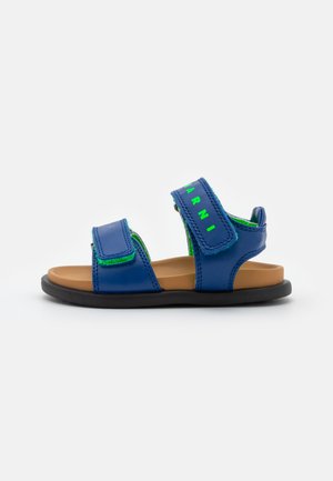 Sandálias azuis com detalhes verdes, feitas de material sintético, apresentando tiras ajustáveis em Velcro e uma sola plana de borracha preta.