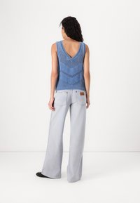 Blauwe gebreide tanktop met een V-hals en een zigzagpatroon, gecombineerd met lichtblauwe wijde spijkerbroek. De outfit heeft een ontspannen, ademend ontwerp.