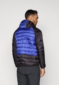 Casaco acolchoado com uma parte superior azul e uma parte inferior preta, com capuz e costuras horizontais para adicionar textura.