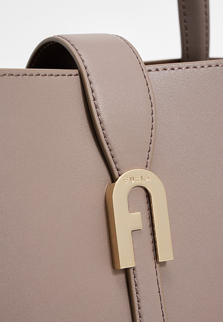 Graue Lederhandtasche mit einem schlanken Design und glatter Textur, akzentuiert mit einem goldfarbenen Metallverschluss. Sichtbare Steppnaht.