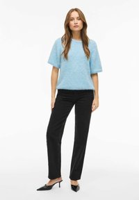 Lyseblå kortermet genser med rund hals, kombinert med svarte bukser med rette ben og spisse svarte hæler.