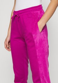 Fuchsia-mjukisbyxor med ribbat mönster på sidan, featuring elastisk midja, dragsko och sidfickor.