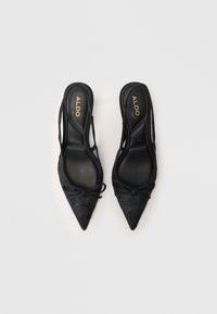 Chaussures à talons italiennes noires, pointues et à dos nu, avec un dessus en tissu texturé, mettant en valeur un accent en nœud et une semelle intérieure noire lisse portant le logo ALDO.