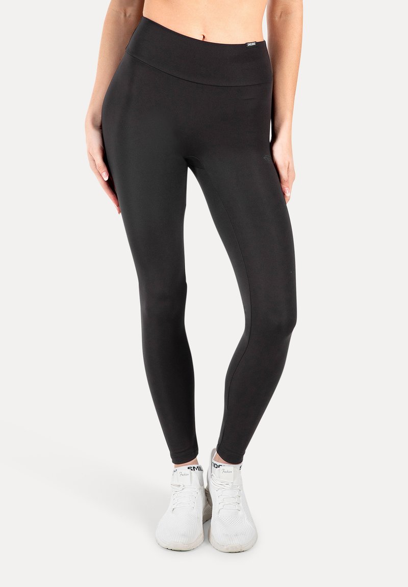 Leggings neri a vita alta realizzati in un tessuto elastico e morbido, con una silhouette aderente, abbinati a scarpe da ginnastica bianche.
