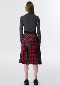Graues langärmliges Oberteil mit gepunkteten Akzenten, kombiniert mit einem roten Tartan-Faltenrock, der mehrfarbige Karomuster und einen schwarzen Bund hat.