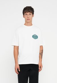 White cotton t-shirt with short sleeves, featuring a teal graphic design on the left chest that reads "NOTES OF NOSTALGIA."
