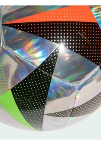 Fotbalový míč s lesklým stříbrným povrchem, který má jasně oranžové, černé a zelené geometrické segmenty s tečkovanými vzory.