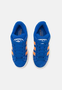 Ténis de camurça azuis com riscas laranja; inclui atacadores planos, colarinho almofadado e o icónico logótipo na lingueta, apresentado numa vista superior.