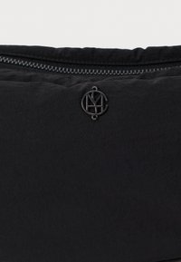Musta nailonipussi, jossa on teksturoitu pintakuvio, yläpään vetskari ja matta musta pyöreä logo koristeena.