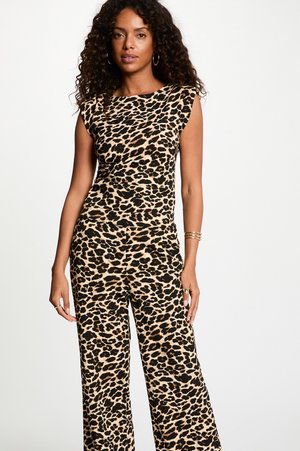 Mujer con cabello rizado que lleva una camiseta sin mangas con estampado de leopardo y pantalones de pierna ancha a juego, complementada con pendientes de aro dorados y pulseras.