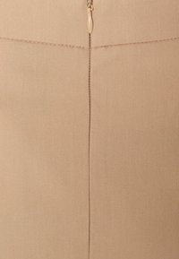 Beige tyg med en slät, strukturerad yta; har en vertikal söm och en dragkedjeslutning i mitten på toppen.