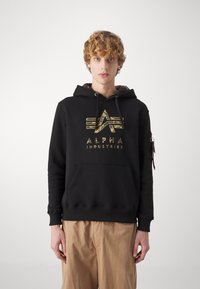 Felpa nera con cappuccio in misto cotone, caratterizzata da un logo mimetico e cappuccio con cordini. Include una tasca frontale a marsupio e una tasca laterale con zip.