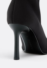 Scarpa nera con tacco alto, in tessuto liscio e elegante, punta affusolata e tacco a stiletto sottile. Design minimalista senza decorazioni.
