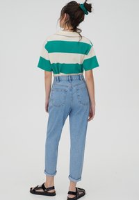 Polo à manches courtes à rayures vertes et crème, associé à un jean clair taille haute et des sandales noires, vu de dos.