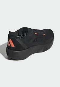 Black athletic shoe with a textured knit upper, featuring perforations for breathability, and orange accents on the heel and tongue.