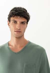 Lichtgroene v-hals t-shirt van zacht materiaal, met een borstzak en een gladde textuur, tegen een effen witte achtergrond.