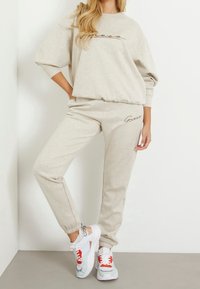 Conjunto de sudadera gris claro que incluye un sudadera de cuello redondo de corte holgado y unos joggers a juego, ambos con acentos de logotipo de la marca bordados. Combinado con zapatillas multicolores.