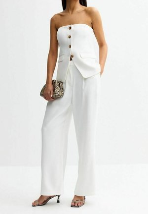 Biały bezramiączkowy kamizelka z guzikami w zestawie z szerokimi białymi spodniami, trzyma kopertówkę ze skóry węża i nosi dopasowane sandały na obcasie.