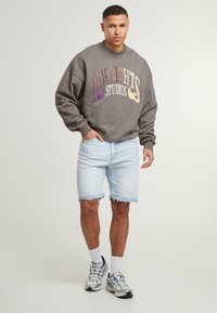 Szürke pulóver, amelyen a "LOWLIGHTS STUDIOS" felirat multikolor betűkkel szerepel, világoskék farmer rövidnadrággal, amelynek szegélyei bolyhosodnak, illetve szürke sportcipővel párosítva.