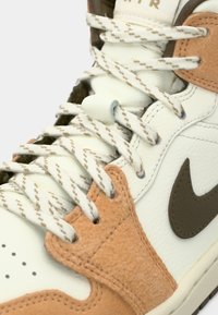 Fehér és barna tornacipő barna Nike pipa logóval, bézs mintás fűzőkkel és részletes varratokkal sima és texturált bőrpaneleken.