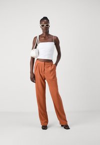 Fehér cropped top vékony pántokkal, narancssárga plisszírozott nadrág, fehér kézitáska és fekete magassarkú szandál; sima textúrák, testhezálló fazon.