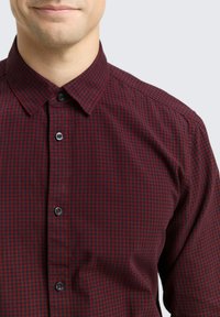 Chemise à carreaux rouge et noire à boutons, en coton, avec un col classique, des boutons noirs et un tissu lisse, légèrement texturé.