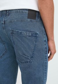 Donkerblauwe denim jeans met een achterzak met een subtiel stikselontwerp en een zwarte leren patch op de tailleband. Gelaagde stof.