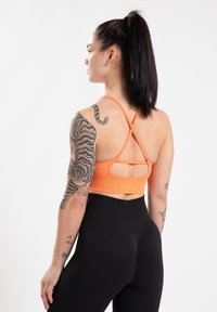 Oranje sportbh met crisscross banden en uitsnijdetail, gecombineerd met hoge zwarte legging met een strakke, gladde textuur.