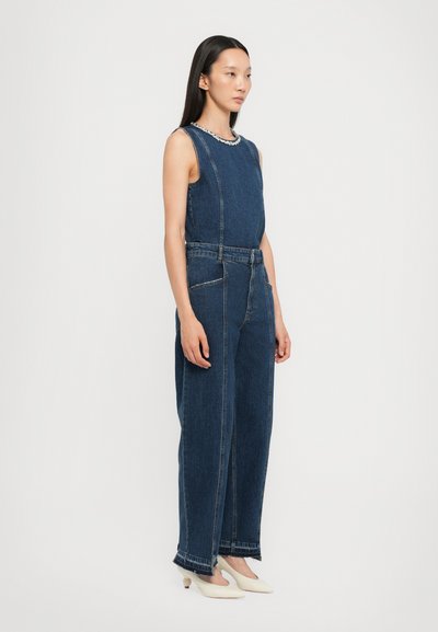 Denim jumpsuit met een mouwloos ontwerp, donkerblauwe kleur, voornaad naden en grote zakken. De randen hebben een ruwe zoom voor een extra detail.