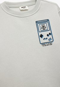Jasnoszara bluza z ribbami na dekolcie, z nadrukiem przypominającym przenośną konsolę do gier z robotem.