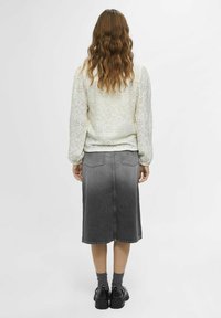 Helle beigefarbene Strickjacke mit strukturiertem Muster und langen Ärmeln, kombiniert mit einem knielangen, grauen Jeansrock und schwarzen klobigen Schuhen.