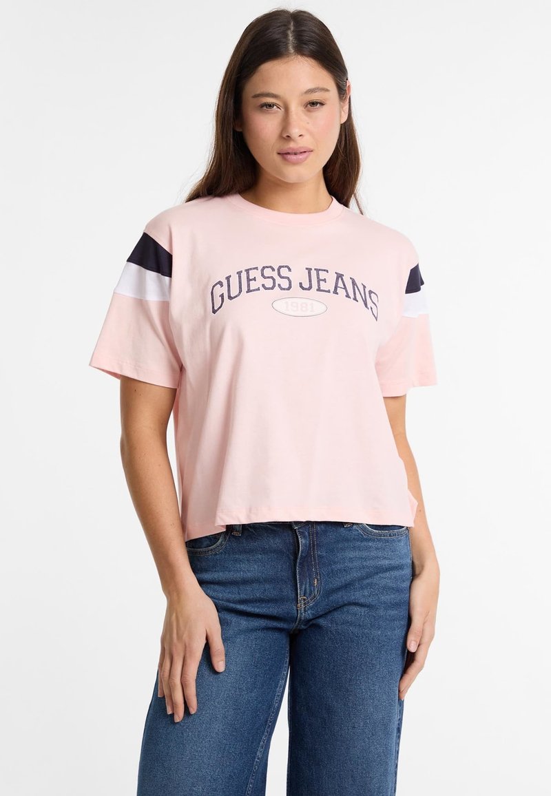 Zastrihnuté ružové tričko s okrúhlym logom "Guess Jeans" a textom 1981, s námorníckymi a bielymi pruhovanými akcentmi na rukávoch.