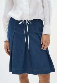 Denim krilo v temno modri barvi s širokim krojem, belim pasom na vrvico in kontrastnim šivanjem ob robu ter naborkih.