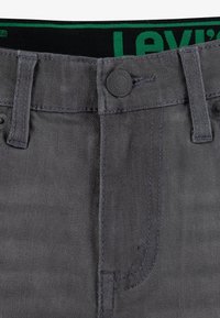 Grå denim jeans har en klassisk knappelukking, kontrasterende sømmer og en merket svart og grønn midje. Glatt tekstur med en lett glans.