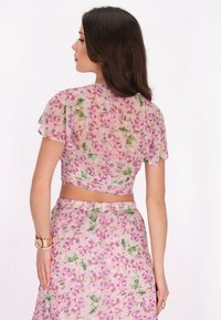 Blumenmuster-Crop-Top und passender Rock aus transparenter Stoff mit rosa- und grünen Blumenmustern; kurze Ärmel und Raffung im Rücken.