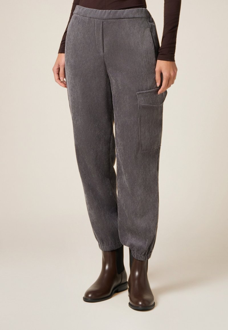 Pantalones de pana gris con una textura suave, que cuentan con un bolsillo lateral y puños elásticos. Llevados con botas de tobillo marrones.