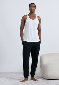 Maiou alb din bumbac și pantaloni negri, cu o croială lejeră. Materialul pare moale, cu o textură fină.