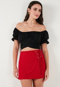 Crna crop top majica bez naramenica s volanima, u kombinaciji s crvenom mini suknjom koja ima bočni vez i glatku teksturu.