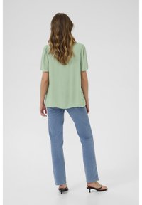 Haut vert clair à manches courtes avec épaules plissées, associé à un jean droit bleu clair et des sandales à talons noires.