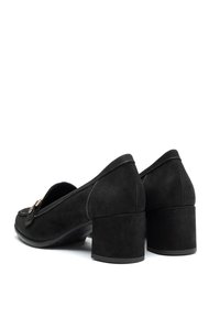 Zapatos de tacón de ante negro con punta redonda, tacón cuadrado, costuras decorativas y un detalle de hebilla en el lateral.