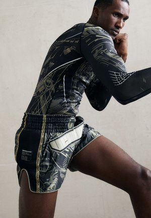 Schwarzes Sportshirt mit komplexen grünen Mustern, kombiniert mit schwarzen und grünen Shorts, die einen strukturierten Bund und Logodetails aufweisen.