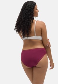 Sostén de maternidad en blanco con tirantes ajustables, acompañado de panties burdeos con terminación de encaje, mostrando una tela suave y una silueta curvada.