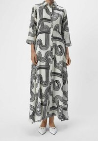 Robe longue à boutonner en tissu léger avec un motif de lignes abstraites noires sur fond blanc. Comprend des manches trois-quarts.