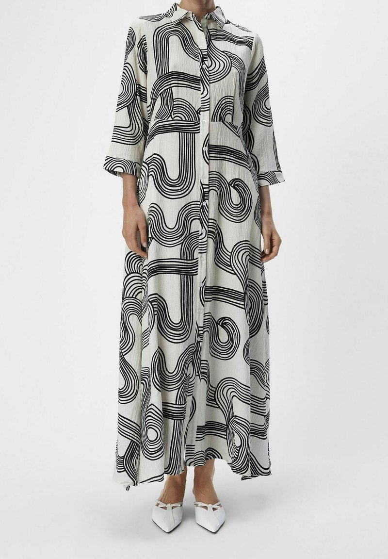 Robe longue à boutonner en tissu léger avec un motif de lignes abstraites noires sur fond blanc. Comprend des manches trois-quarts.