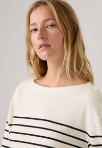Cremfarbener Oberteil mit schwarzen horizontalen Streifen, weitem Ausschnitt, strukturiertem Stoff und überschnittenen Schultern. Schlichtes, lässiges Design.
