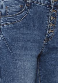 Koptatott kék farmernadrág texturált felülettel. Fém gombos záródással és ötlovas zsebes kialakítással, kontrasztos varrással.