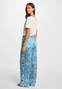 T-shirt bianco a maniche corte abbinato a pantaloni svasati blu con motivo a fantasia che presenta intricati motivi floreali verdi e bianchi e una vita elastica.